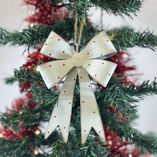 White Metal Bow Ornament with red polka dots and a twine hanger, hanging on a green Christmas tree with red tinsel
