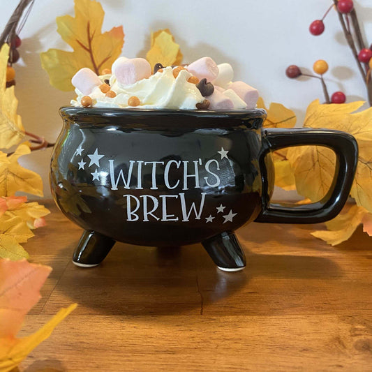 Black witch's brew mug with hot chocolate, marshmallows, and autumn leaf decor