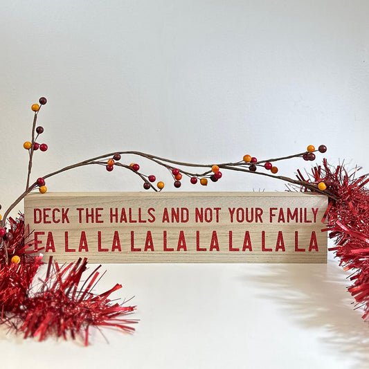 'Deck The Halls' Wooden Sign standing on a white shelf with a berry sprig and red tinsel