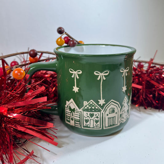 Green Bow Christmas Mug, a green stoneware mug with white bows and a house pattern, on red tinsel