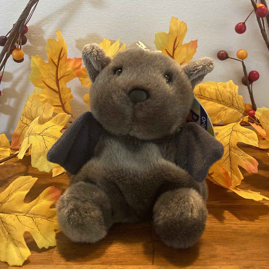 Palm Pals Luna the Halloween Bat plush toy sitting among autumn leaves