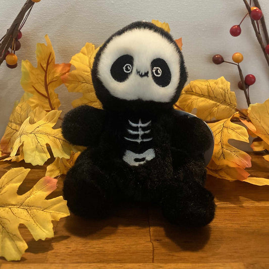 Palm Pals Skelly the Skeleton plush toy sitting among autumn leaves