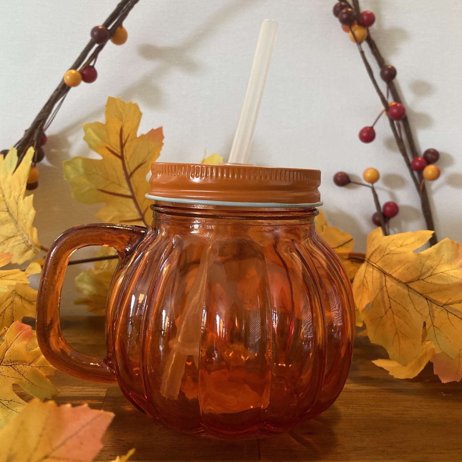 Pumpkin-shaped glass tumbler with lid and straw, front view with autumn leaf decor