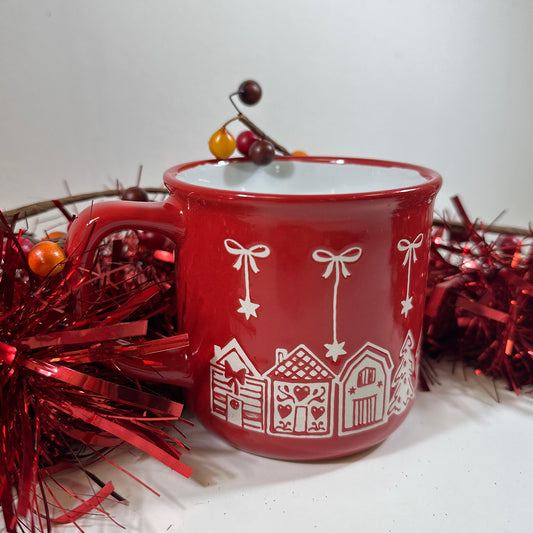 Red Bow Christmas Mug, a red stoneware mug with white bows and a house pattern, on red tinsel