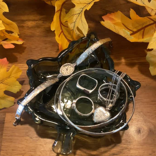 Sage glass leaf trinket dish holding rings, a watch, bracelets, and a necklace